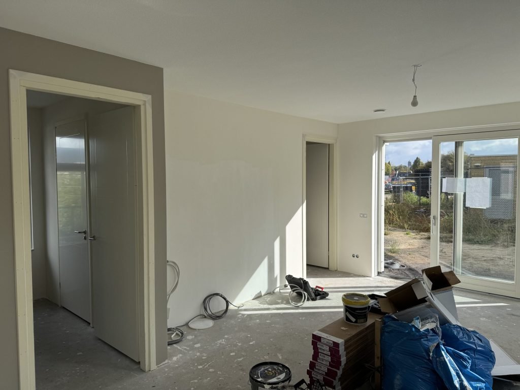Woonkamer van een nieuwbouwwoning tijdens de afwerking, met emmers en dozen materiaal op de betonvloer