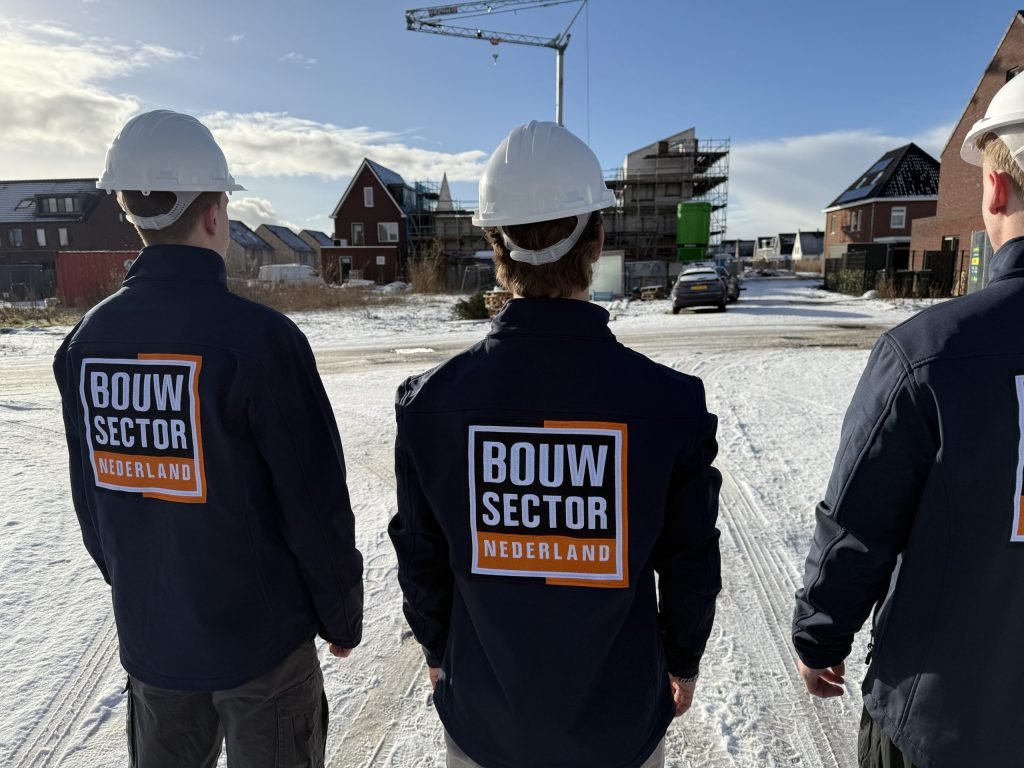 Drie vakmensen van Bouwsector Nederland met witte helm op een besneeuwde straat met huizen in aanbouw